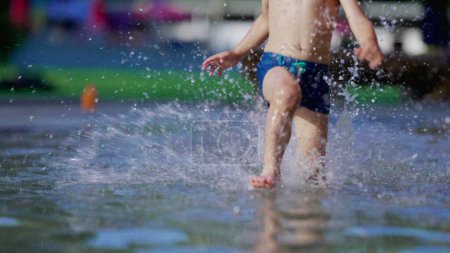 Photo for Joyful child running in swimming pool water splashing water in slow-motion during summer day. Active little boy sprinting at 120fps - Royalty Free Image