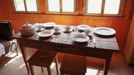 Foto de Vajilla de cerámica clásica en entorno pastoral. Platos blancos, tazas de té y utensilios expuestos en una mesa de madera vieja - Imagen libre de derechos