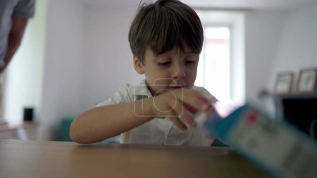 Téléchargez les photos : Un petit garçon ouvre une boîte cadeau. Enfant recevant un cadeau d'anniversaire avec impatience. Enfant essayant de déchirer la boîte à jouets - en image libre de droit
