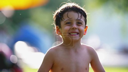Foto de Retrato de niño pequeño sentado en la hierba al aire libre después de nadar en la piscina, expresión relajada y feliz, cálido día de verano - Imagen libre de derechos