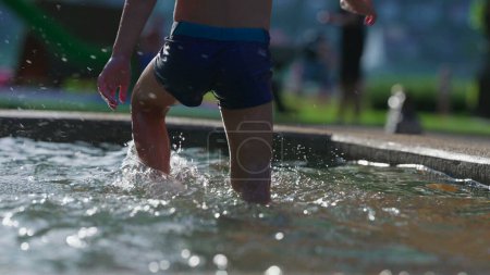 Téléchargez les photos : Petit garçon se rafraîchissant à la piscine publique pendant l'activité de jour d'été. Enfant marchant dans la piscine éclaboussant l'eau en 120fps au ralenti - en image libre de droit