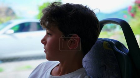 Téléchargez les photos : Profil de jeune garçon voyageant en bus regardant passer la vue. Enfant adolescent contemplatif rêvant pendant son voyage en transport - en image libre de droit