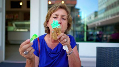 Photo for Senior Lady Relishing a Cold Ice-Cream Treat on a Sunny Day at Parlor Shop. Older woman savoring waffle cone dessert - Royalty Free Image