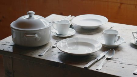 Foto de Platos blancos tradicionales, utensilios, tazas de té, sencillos y humildes. Mesa de madera, tazón de cerámica. Entorno rural rústico - Imagen libre de derechos