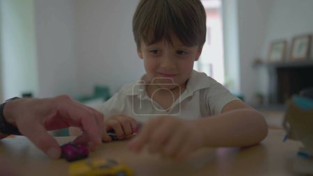 Téléchargez les photos : Petit garçon saisissant des véhicules jouets de table après avoir déballé le cadeau. Enfant joue avec des jouets automobiles - en image libre de droit