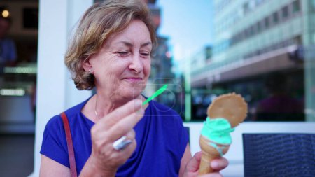Photo for Happy Senior woman enjoying ice-cream cone outside at parlor shop. Older person eating sweet dessert treat - Royalty Free Image