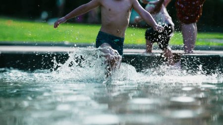 Foto de Alegre niño corriendo a través del agua de la piscina en el día de verano, chico energético haciendo salpicaduras mientras corre en cámara lenta 120fps en la piscina - Imagen libre de derechos