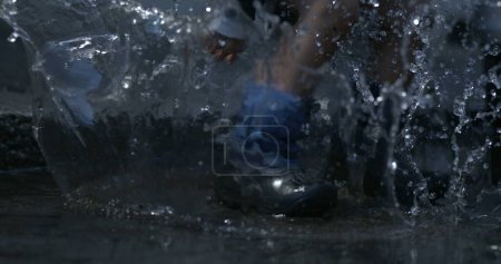 Foto de Alegre niño salpicadura acera charco a 800 fps, gotas de agua se elevan por todas partes - Imagen libre de derechos