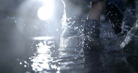 Téléchargez les photos : Enfant en bottes de pluie se précipitant dans la flaque d'eau avec un effet spectaculaire de gouttelettes au ralenti - en image libre de droit