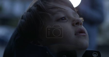 Foto de Cara de primer plano del niño pensativo reflexivo mirando hacia arriba con expresión en blanco en la hora del atardecer por la tarde - Imagen libre de derechos