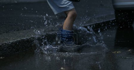 Photo for Child jumping into puddle in the street with rainboots in super slow-motion at 800 fps captured in high-speed, splashing water everywhere - Royalty Free Image
