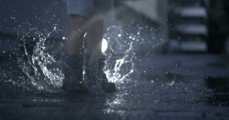 Foto de Niño en ropa de lluvia en el aire sobre charco con captura detallada de salpicaduras en cámara lenta - Imagen libre de derechos