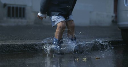 Photo for Splash Symphony - Energetic Kid in Rainboots Sends Water Droplets Flying at 800 fps on Sidewalk - Royalty Free Image