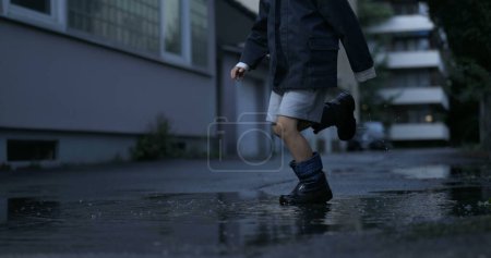 Photo for Nostalgic scene of child kicking puddle of water in street alley having fun by himself filmed in high-speed camera - Royalty Free Image