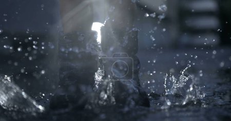 Photo for Nostalgic scene of child wearing rain boots jumping in the air in water puddle having fun in ultra slow-motion captured in high-speed camera - Royalty Free Image