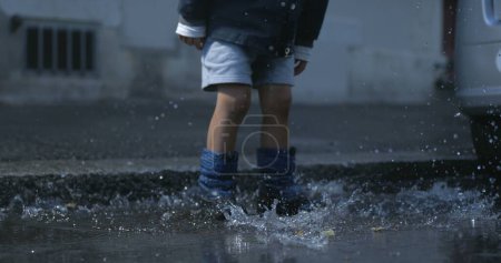 Photo for Splash Symphony - Energetic Kid in Rainboots Sends Water Droplets Flying at 800 fps on Sidewalk - Royalty Free Image