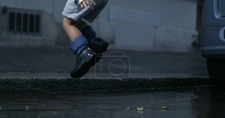 Photo for Child splashing water everywhere falling into puddle in street wearing rainboots in high-speed camera at 800 fps - Royalty Free Image