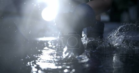 Téléchargez les photos : Enfant en bottes de pluie se précipitant dans la flaque d'eau avec un effet spectaculaire de gouttelettes au ralenti - en image libre de droit