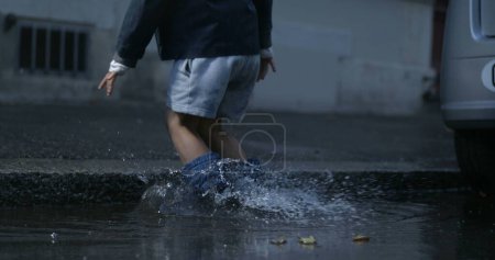 Photo for Child splashing water everywhere falling into puddle in street wearing rainboots in high-speed camera at 800 fps - Royalty Free Image