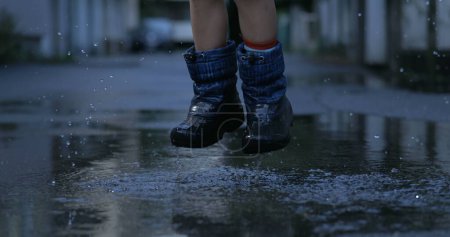 Foto de Divertido niño caminando en charcos de agua salpica gotas de agua en cámara lenta en todas partes capturado en alta velocidad 800 fps - Imagen libre de derechos