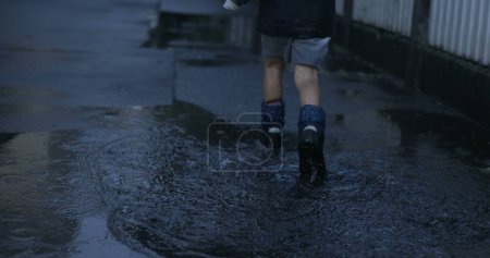 Photo for Kid joyfully sprinting in rain boots into puddle with super slow-motion splash - Royalty Free Image