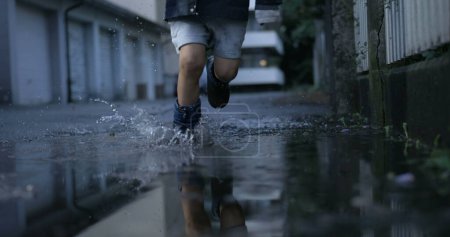 Photo for Joyful child sprinting in water puddles splashing water in the air captured with high-speed camera in ultra slow-motion - Royalty Free Image