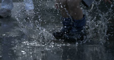 Téléchargez les photos : Puddle Playtime - Les sauts de pluie énergiques de l'enfant provoquent des éclaboussures d'eau et une capture à grande vitesse un jour de pluie - en image libre de droit