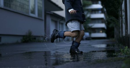 Téléchargez les photos : Puddle de coups de pied d'enfant de l'eau avec des bottes de pluie créant éclaboussures capturées au ralenti super à 800 ips avec une caméra à grande vitesse - en image libre de droit