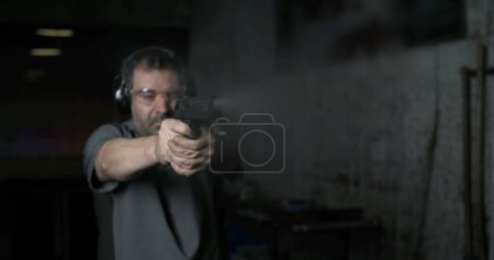 Photo for Man aiming and firing with Desert Eagle gun in high-speed slow-motion at 800 fps at shooting range training. Person practicing with weapon - Royalty Free Image