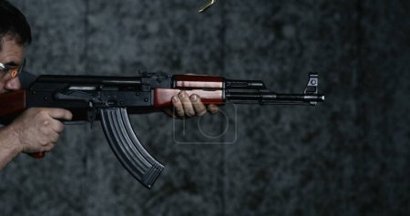 Foto de Vista lateral de la persona que dispara un rifle AK-47 en alta velocidad 800 fps. Lento movimiento del hombre apuntando y disparando Kalashnikov - Imagen libre de derechos