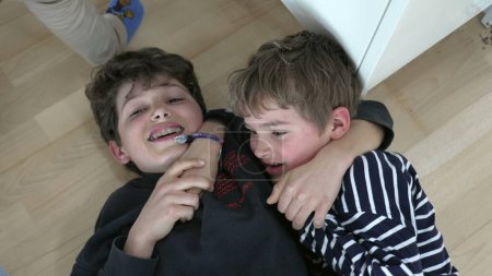Photo for Brothers fighting each other laid on floor, wrestling. Siblings quarreling, family rivalry - Royalty Free Image
