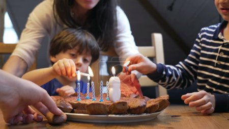 Photo for Birthday scene celebration, children lighting candles during 8 year old boy celebration. two brothers in front of cake - Royalty Free Image