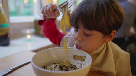 Foto de Un niño comiendo espaguetis en un tazón. Muchacho hambriento disfrutando de comida en el restaurante - Imagen libre de derechos
