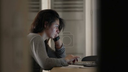 Photo for Woman browsing internet in front of laptop at home, candid authentic scene of person in front of computer screen late at night - Royalty Free Image