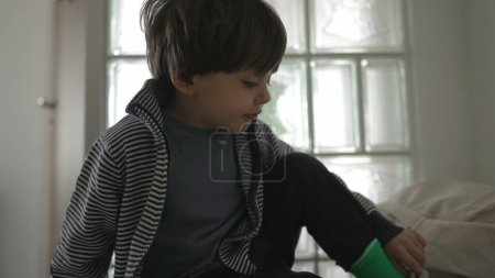 Photo for Small boy putting on shoes by door front entrance, child preparing to go out puts shoe, getting ready to go out - Royalty Free Image