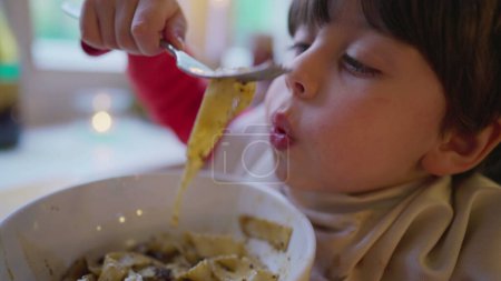 Foto de Niño con servilleta metida en el cuello, deleitándose con espaguetis en el restaurante. Niño comiendo comida de pasta - Imagen libre de derechos