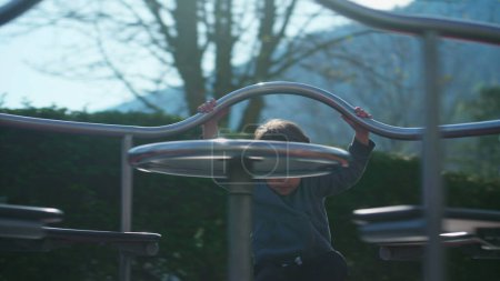 Téléchargez les photos : Jeune garçon jouant joyeusement sur le carrousel à l'aire de jeux tournant d'une manière insouciante, Petit garçon s'amusant délicieusement sur le rond-point du parc - en image libre de droit