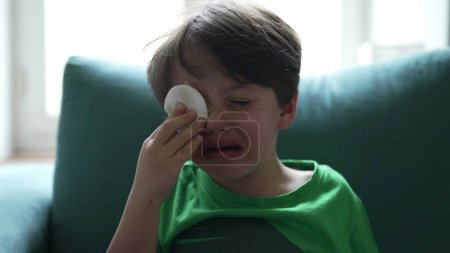 Photo for Crying small boy with hurt eye emergency, open mouth tearful child feeling pain after accident, hand covering eye with cotton - Royalty Free Image