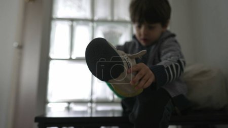 Foto de Calzado Frustration Little Boy Resisting Socks and Shoes by Doorway. Niño irritado mientras trata de vestirse, preparándose para salir - Imagen libre de derechos
