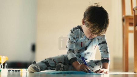 Téléchargez les photos : Créativité tôt le matin - Enfant en pyjama Croquis avec stylo bleu sur le sol - en image libre de droit