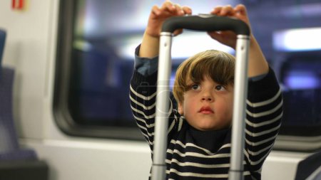 Foto de Pequeño pasajero jugando con el asa superior de la maleta. juego en solitario del niño que pasa el tiempo mientras viaja en tren - Imagen libre de derechos