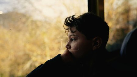 Photo for Melancholic young boy staring at train view with sad depressed expression, child travels by railroad with thoughtful pensive expression - Royalty Free Image