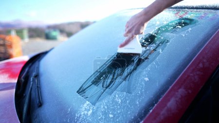 Photo for Close-up hand Removing frost from car windshield glass with ice scraper, preparing for road trip commute during winter season - Royalty Free Image