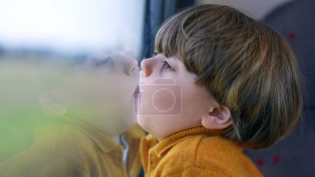 Foto de Aburrido niño pequeño divertido con la cara pegada en la ventana triana. Boca y labios presionados sobre el vidrio y mirando el paisaje pasan en el transporte - Imagen libre de derechos