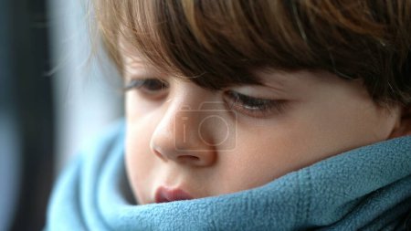 Photo for Pensive child close-up face in deep thoughtful emotion wearing scarf. One little caucasian boy lost in thought - Royalty Free Image