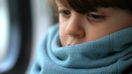 Foto de Cara de niño pensativo de cerca en profunda emoción reflexiva con bufanda. Un pequeño chico caucásico perdido en el pensamiento - Imagen libre de derechos