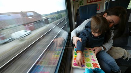 Photo for Diligent mom imparting lessons to son during train journey, child engaging in educational tasks with parent amidst commute - Royalty Free Image