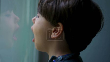 Téléchargez les photos : Enfant respirant de l'air dans le verre de fenêtre créant condensation, moment d'enfance ludique - en image libre de droit