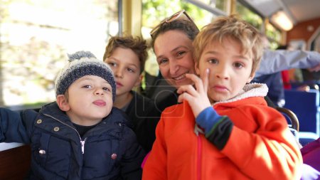 Foto de Madre e hijos montando tren yendo a las montañas, mamá rodeada de niños pequeños viajando en transporte mirando la cámara posando y sonriendo - Imagen libre de derechos