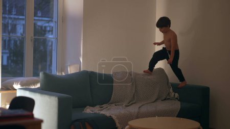 Téléchargez les photos : Enfant franc jouant la nuit sur le canapé, courant énergiquement le soir en s'amusant seul le soir - en image libre de droit